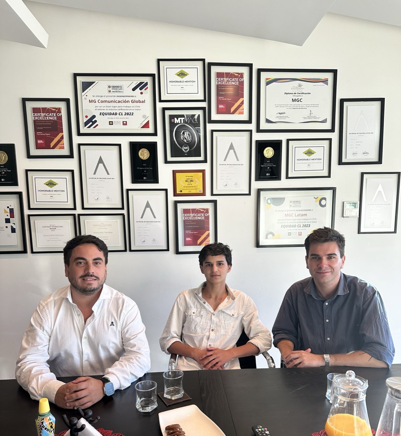 Three people seated in front of an awards wall